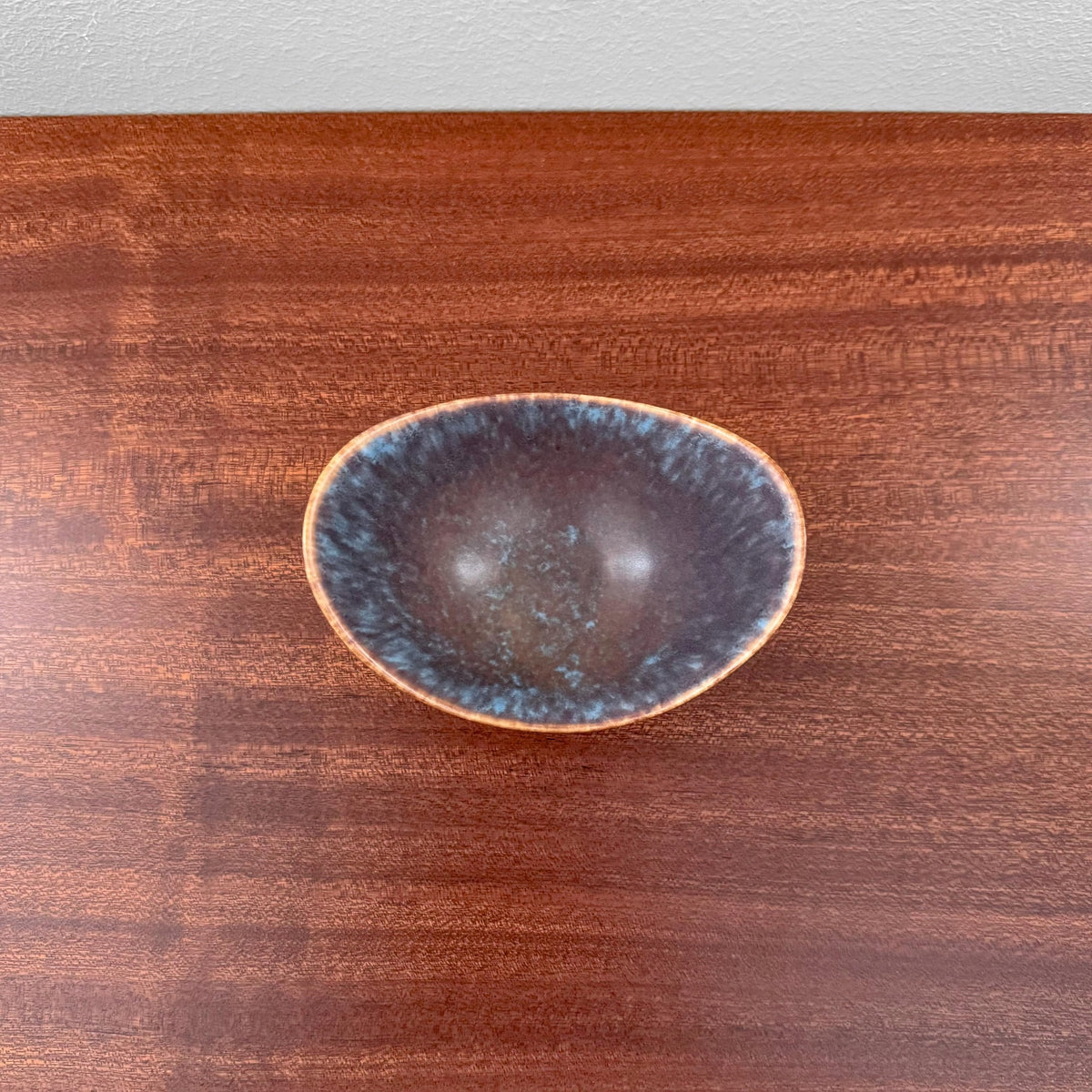 Gunnar Nylund Rörstrand ARO Small Stoneware Decorative Bowl in blue and brown glaze with organic shape, vintage 1950s-60s Scandinavian ceramic piece on wooden surface.