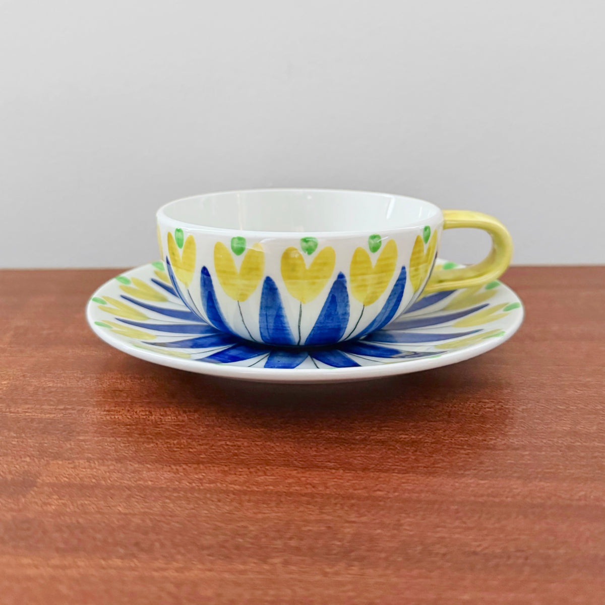 Hertha Bengtson Rörstrand Tea Cup with Saucer featuring a vibrant yellow and blue floral design on ceramic, showcasing vintage Scandinavian craftsmanship from the 1940s.