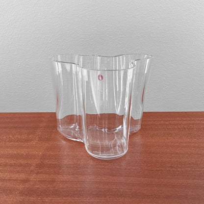 Iittala Aalto Savoy Clear Glass Vase (120 mm) designed by Alvar Aalto, featuring a fluid organic shape crafted in clear glass, displayed on a wooden surface.