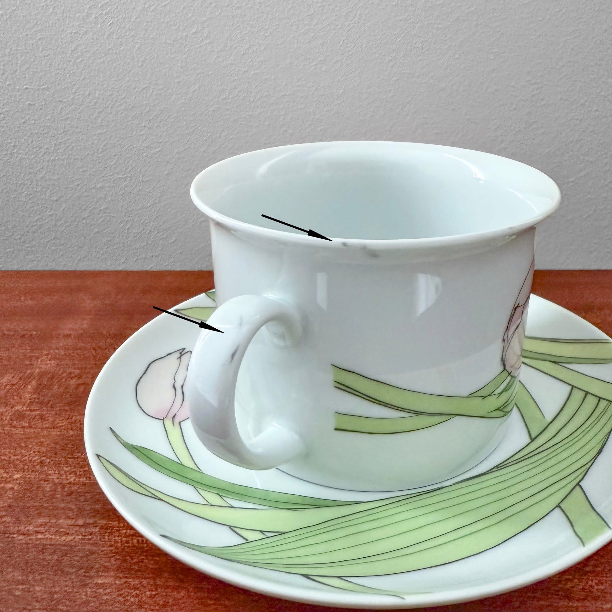 IKEA Näckros Large Tea Cup with Saucer featuring a delicate floral design, made of ceramic with minor blemishes on the rim and handle, displayed on a wooden surface.