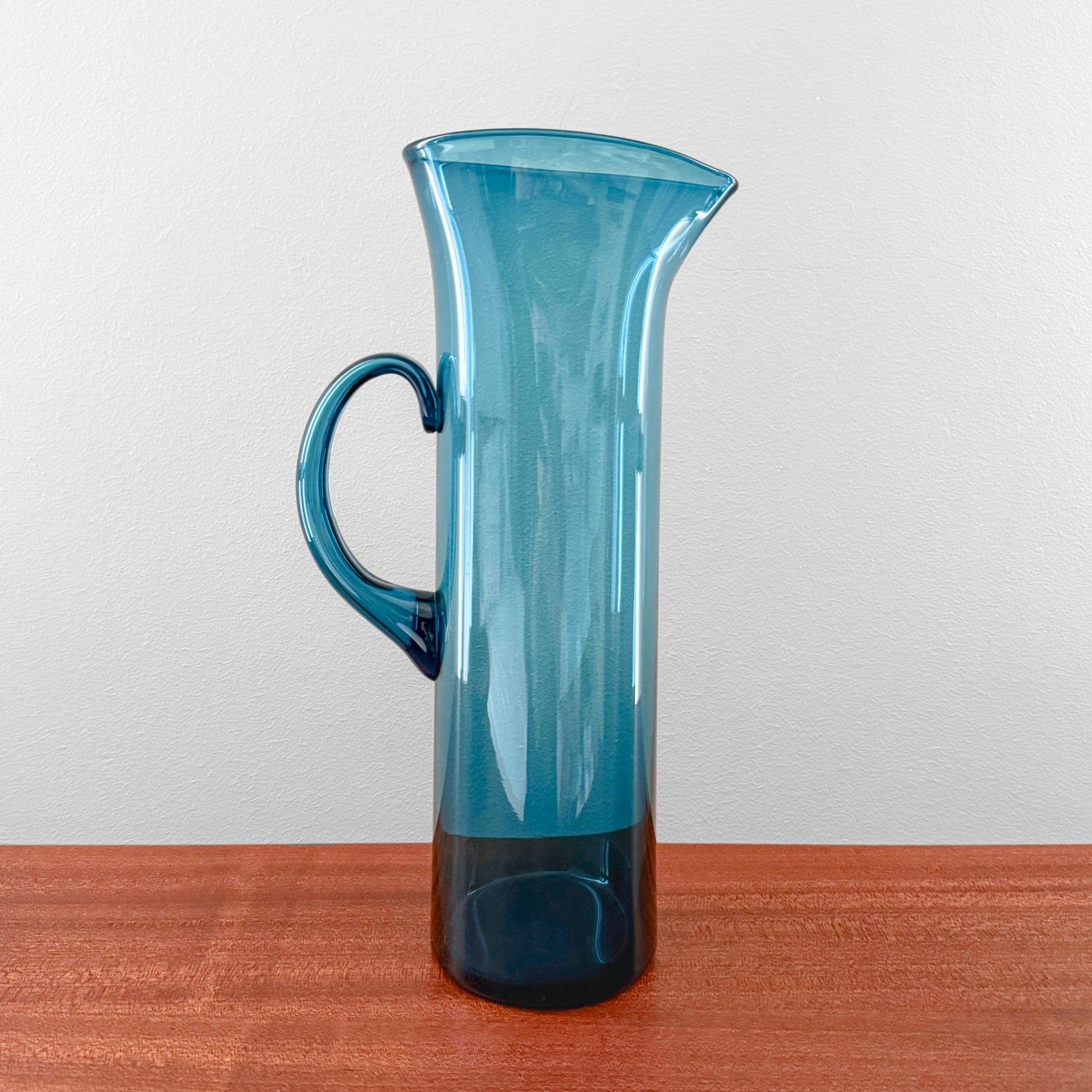 Ingeborg Lundin Orrefors Blue Glass Pitcher with a tall, slender form, curved handle, and deep blue vintage Scandinavian glass design sitting on a wooden surface.
