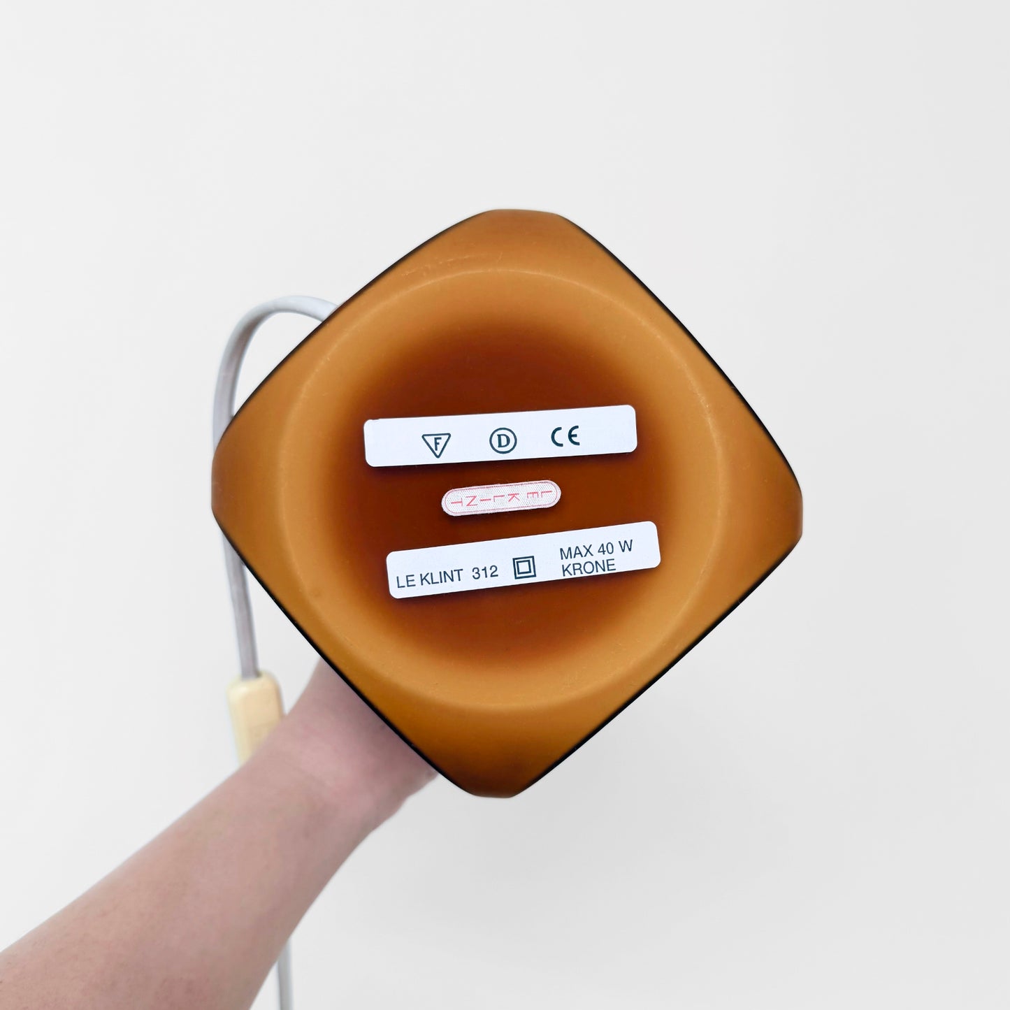 Bottom view of Le Klint 312 Amber Opal Glass Table Lamp showing amber colored glass base with labels and electrical cord attached, highlighting vintage Nordic lighting design.