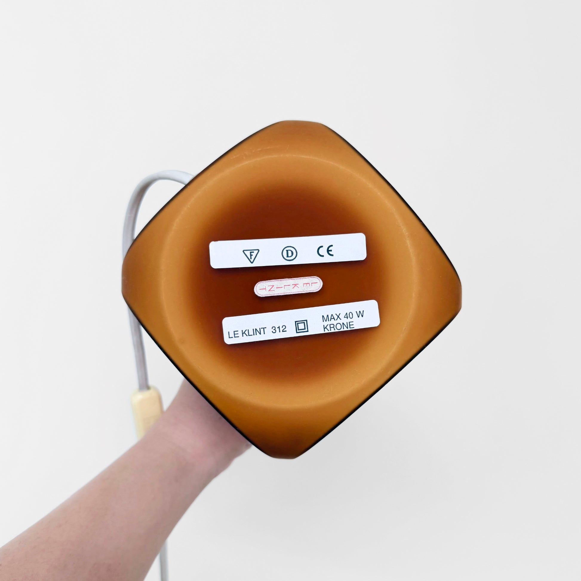 Bottom view of Le Klint 312 Amber Opal Glass Table Lamp showing amber colored glass base with labels and electrical cord attached, highlighting vintage Nordic lighting design.