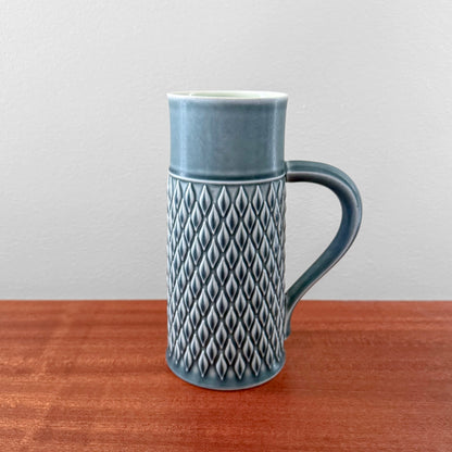 Quistgaard Relief Azure Pitcher in rare vintage azure color with textured diamond relief pattern and curved handle, displayed on wooden surface against a plain background.