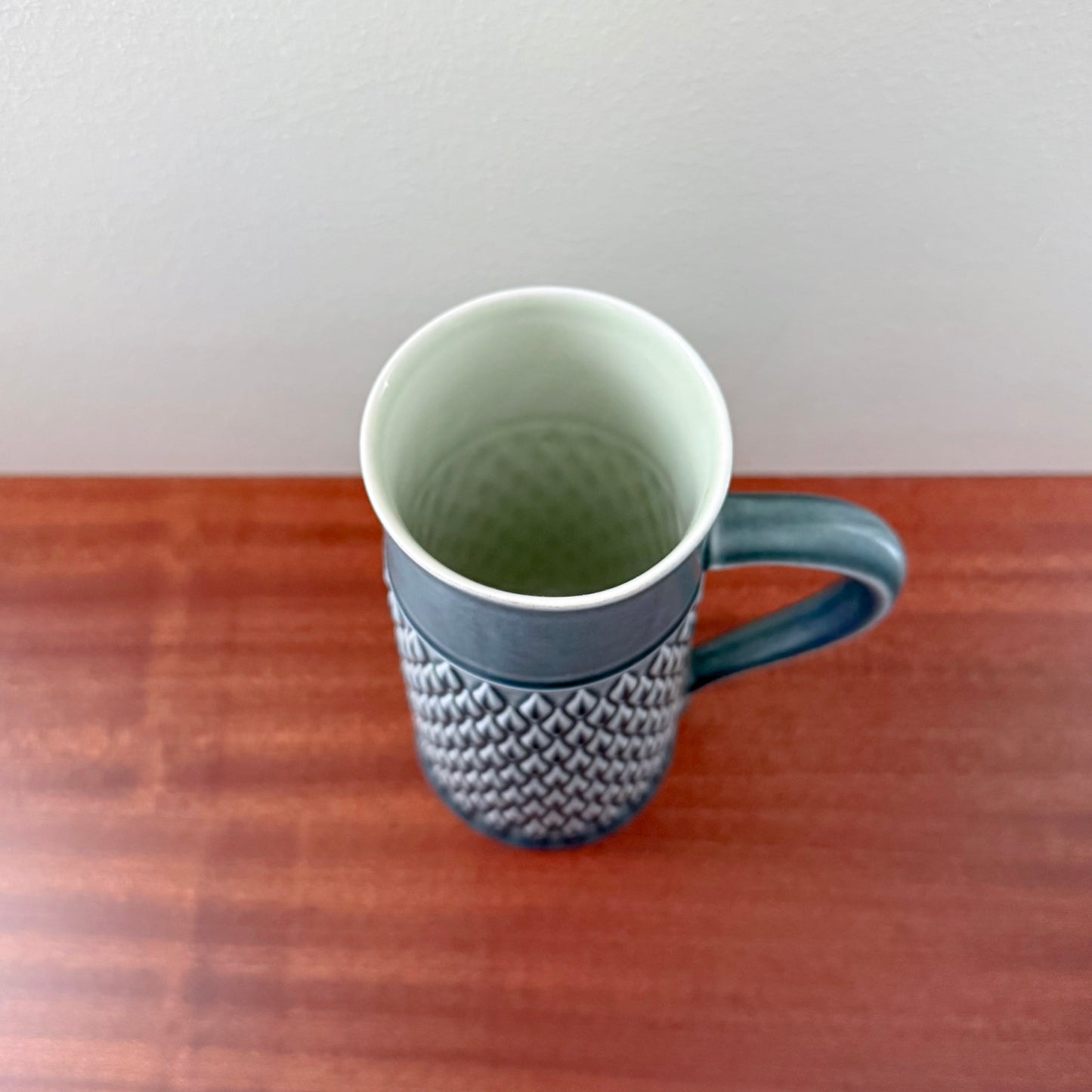 Top view of a Quistgaard Relief Azure Pitcher with intricate textured pattern and blue handle on a wooden surface against a plain white background.