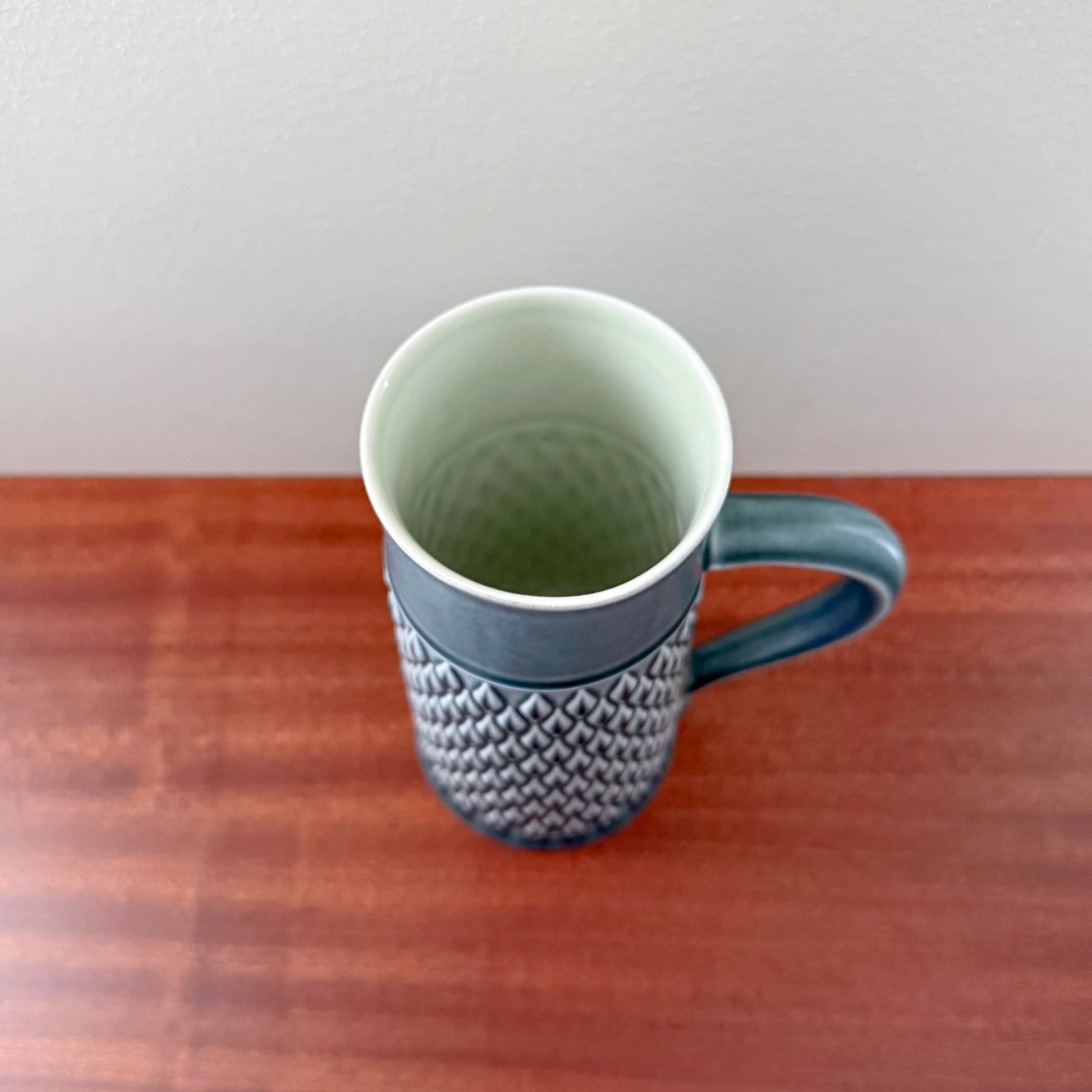 Top view of a Quistgaard Relief Azure Pitcher with intricate textured pattern and blue handle on a wooden surface against a plain white background.