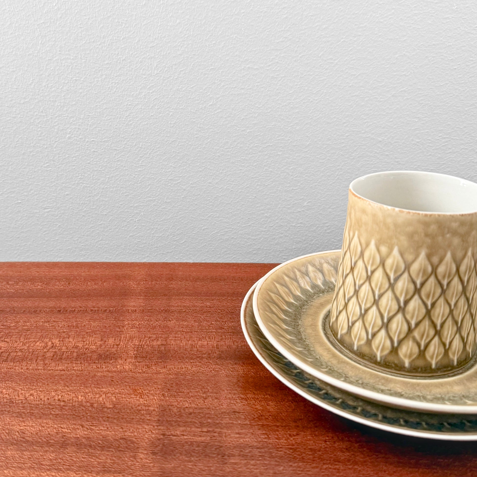 Quistgaard Relief Coffee Cup Trio Set featuring a textured ceramic coffee cup, matching saucer and cake plate in warm beige tones on a wooden surface.