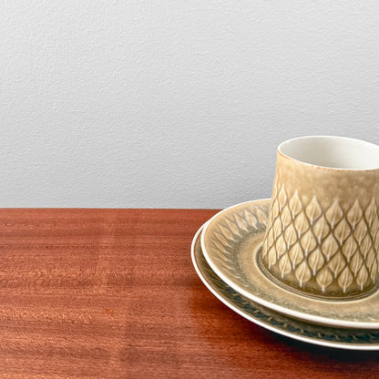 Quistgaard Relief Coffee Cup Trio Set featuring a textured ceramic coffee cup, matching saucer and cake plate in warm beige tones on a wooden surface.