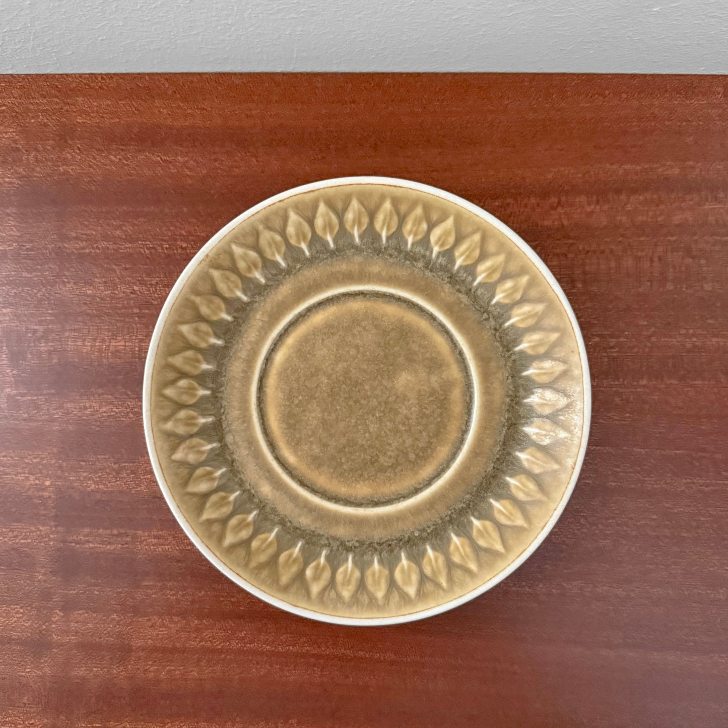 Quistgaard Relief Coffee Cup Trio Set saucer with embossed leaf pattern in muted earth tones on wooden surface, vintage Nordic ceramic drinkware.