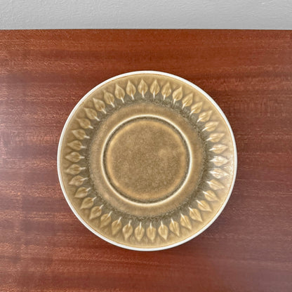 Quistgaard Relief Coffee Cup Trio Set saucer with embossed leaf pattern in muted earth tones on wooden surface, vintage Nordic ceramic drinkware.