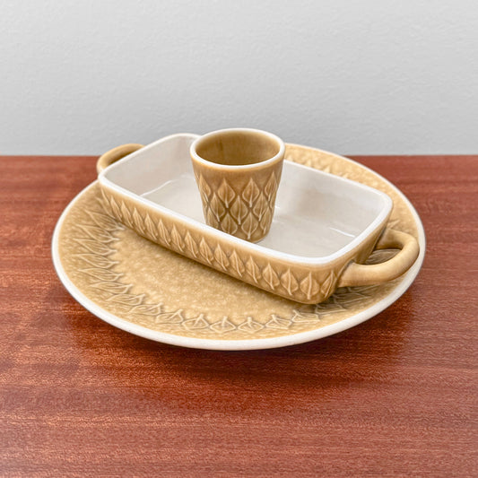 Quistgaard Relief Tableware Set with beige ceramic large cake plate, rectangular oven dish with handles, and matching egg cup featuring textured relief pattern.