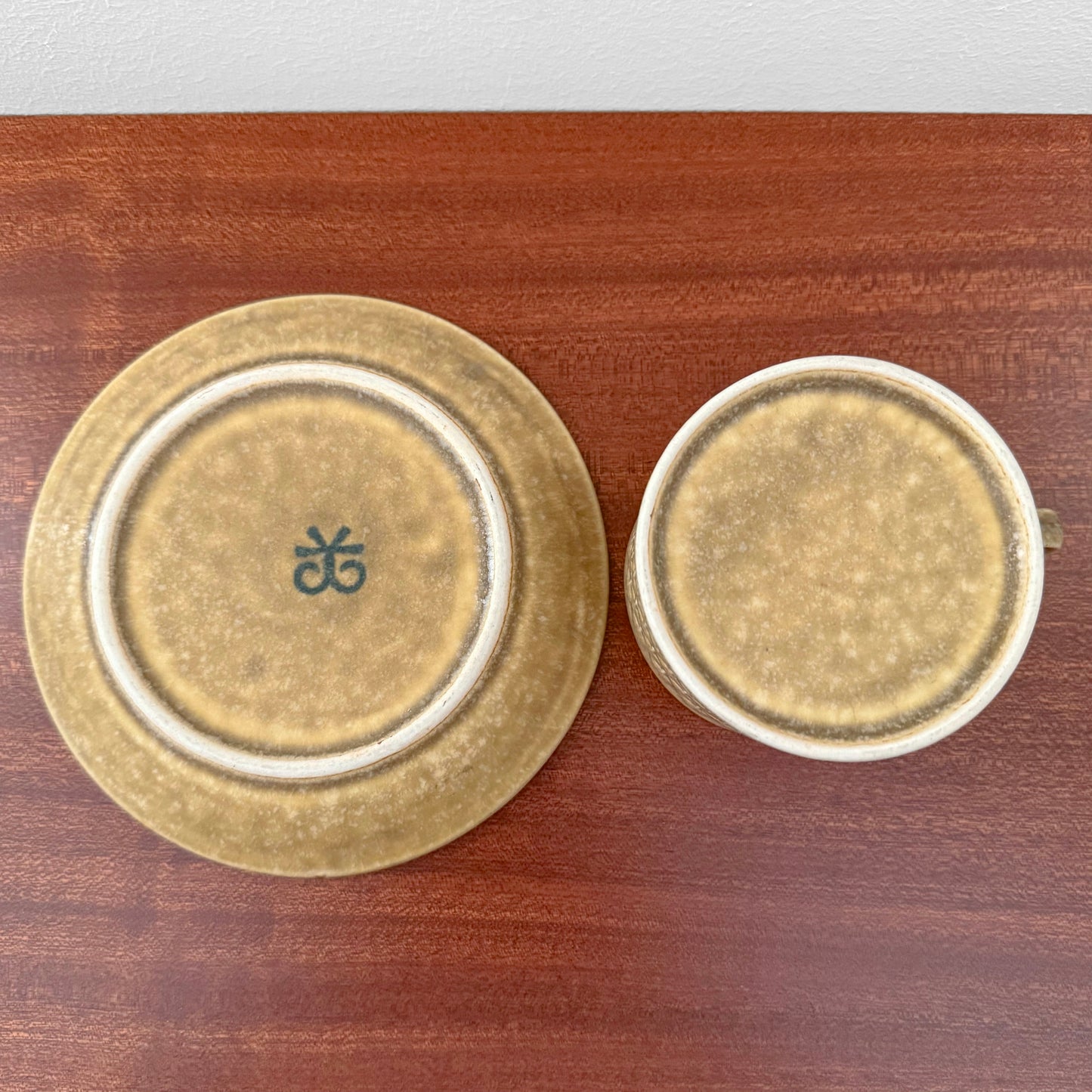 Quistgaard Relief Tea Cup Trio Set with Large Cake Plate showing bottom view of cup and saucer with textured brown glaze on wooden surface, vintage Nordic drinkware.
