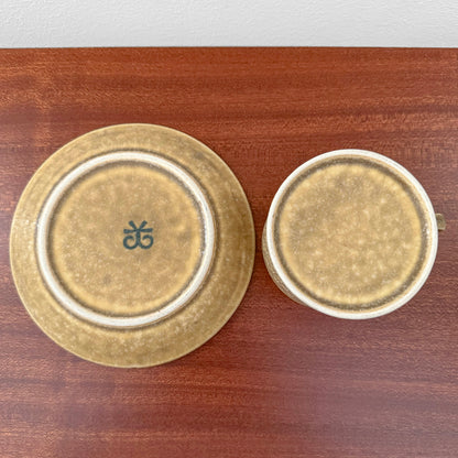 Quistgaard Relief Tea Cup Trio Set with Large Cake Plate showing bottom view of cup and saucer with textured brown glaze on wooden surface, vintage Nordic drinkware.