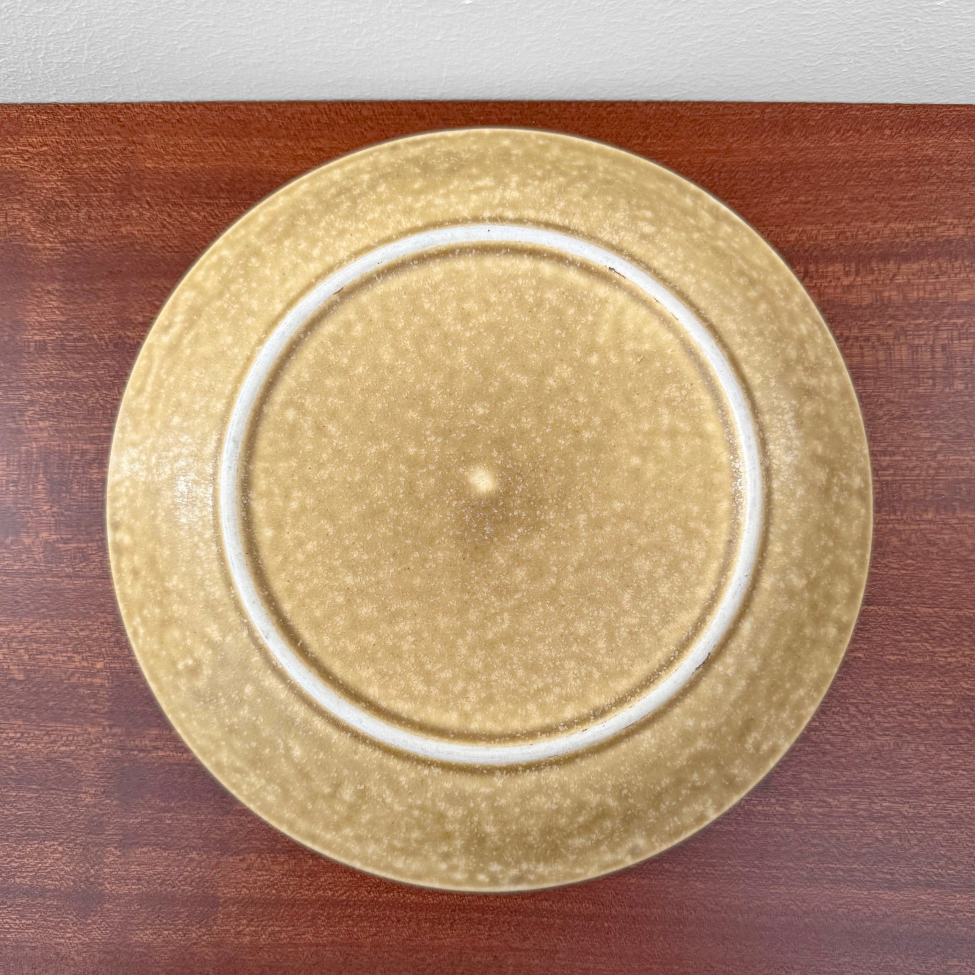 Quistgaard Relief Tea Cup Trio Set with Large Cake Plate showcasing a vintage ceramic cake plate with textured beige glaze on a wooden surface.