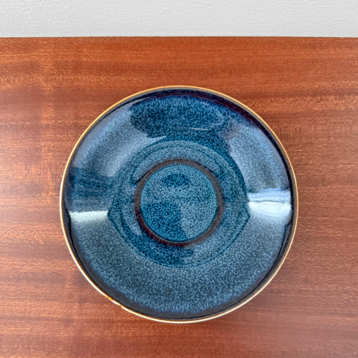 Rörstrand Litorina Blue Tea Cup with Saucer featuring a blue glazed ceramic cake plate with concentric rings and a gold rim on a wooden surface