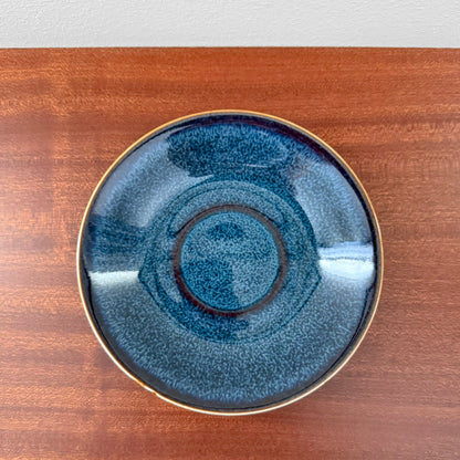 Rörstrand Litorina Blue Tea Cup with Saucer featuring a blue glazed ceramic cake plate with concentric rings and a gold rim on a wooden surface