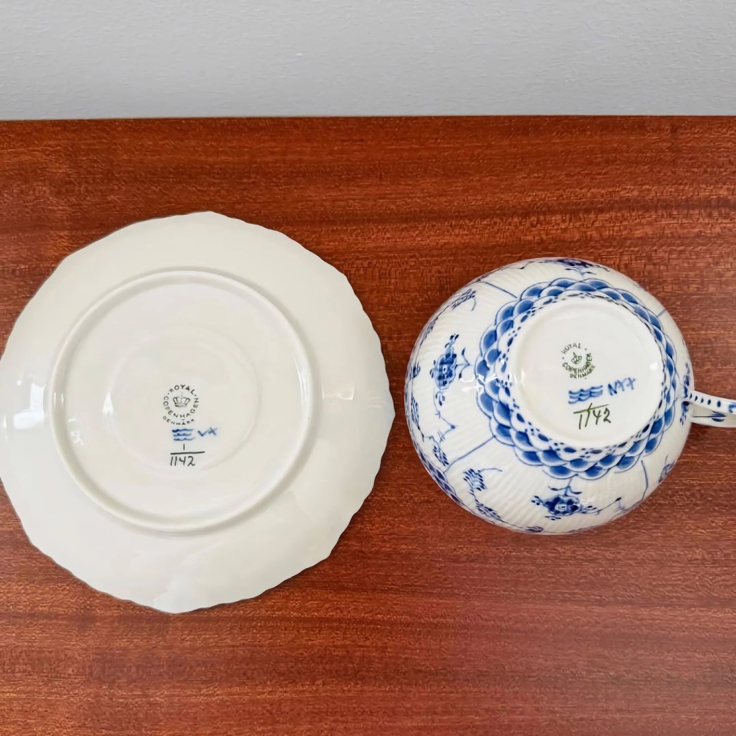 Bottom view of the Royal Copenhagen Blue Fluted Full Lace Large Tea Cup Trio Set showing the ceramic marks and intricate blue floral patterns on the cup and the saucer on a wooden surface.