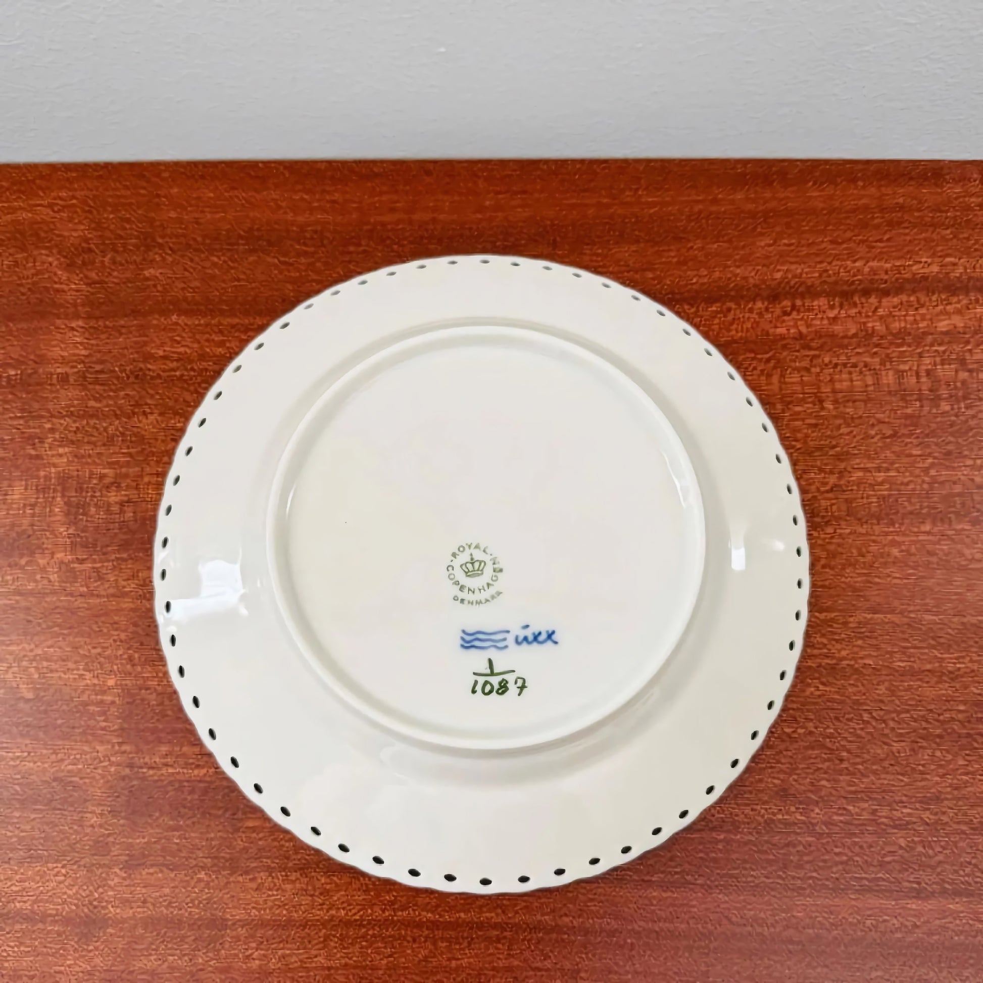 Back view of a ceramic cake plate from the Royal Copenhagen Blue Fluted Full Lace Large Tea Cup Trio Set showing maker's marks and decorative scalloped edge on wood surface.