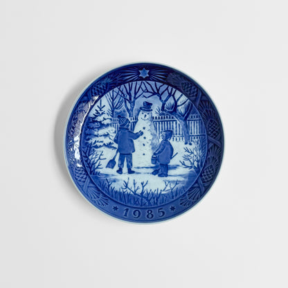 Royal Copenhagen Christmas Plates decorative dish in blue and white with children building a snowman in a winter scene and 1985 date around the rim