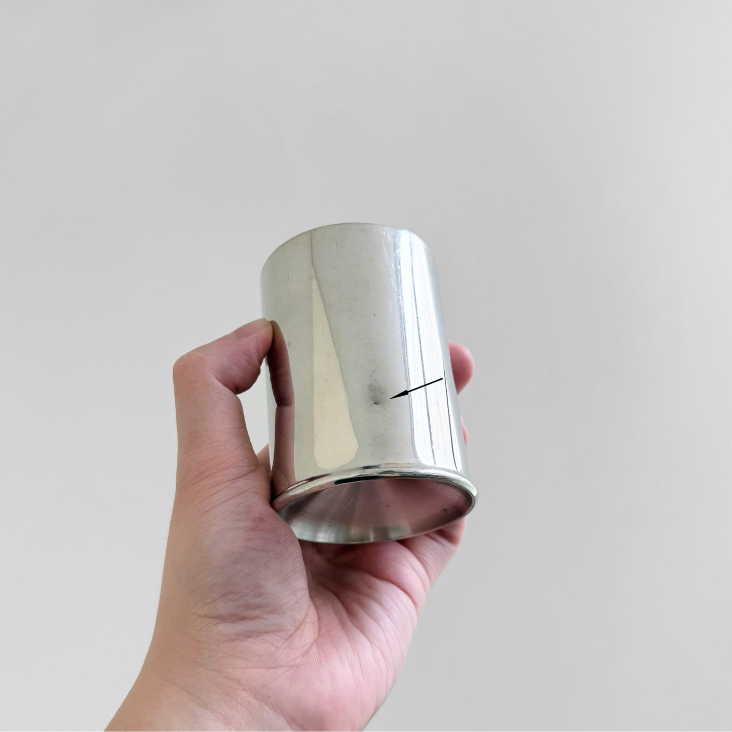 Hand holding a polished pewter cup from the Royal Selangor Erik Magnussen Pewter Coffee Set, showcasing its smooth reflective surface and minimalistic design.