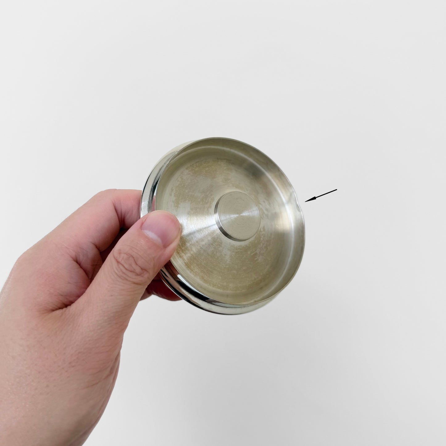 Hand holding a round pewter lid with small dents and signs of vintage use from the Royal Selangor Erik Magnussen Pewter Coffee Set against a plain white background.