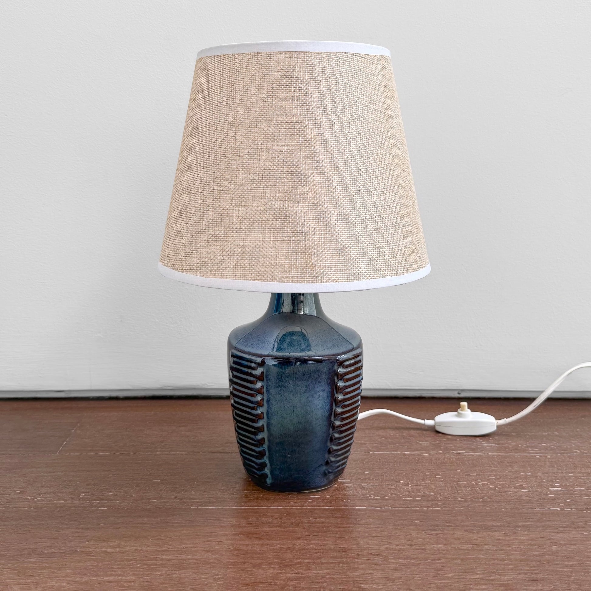 Søholm 1025 Blue Stoneware Table Lamp with ceramic blue glazed base featuring textured vertical ridges and a beige fabric shade on a wooden surface.