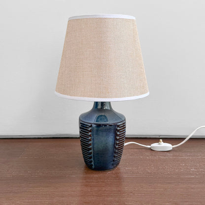 Søholm 1025 Blue Stoneware Table Lamp with ceramic blue glazed base featuring textured vertical ridges and a beige fabric shade on a wooden surface.