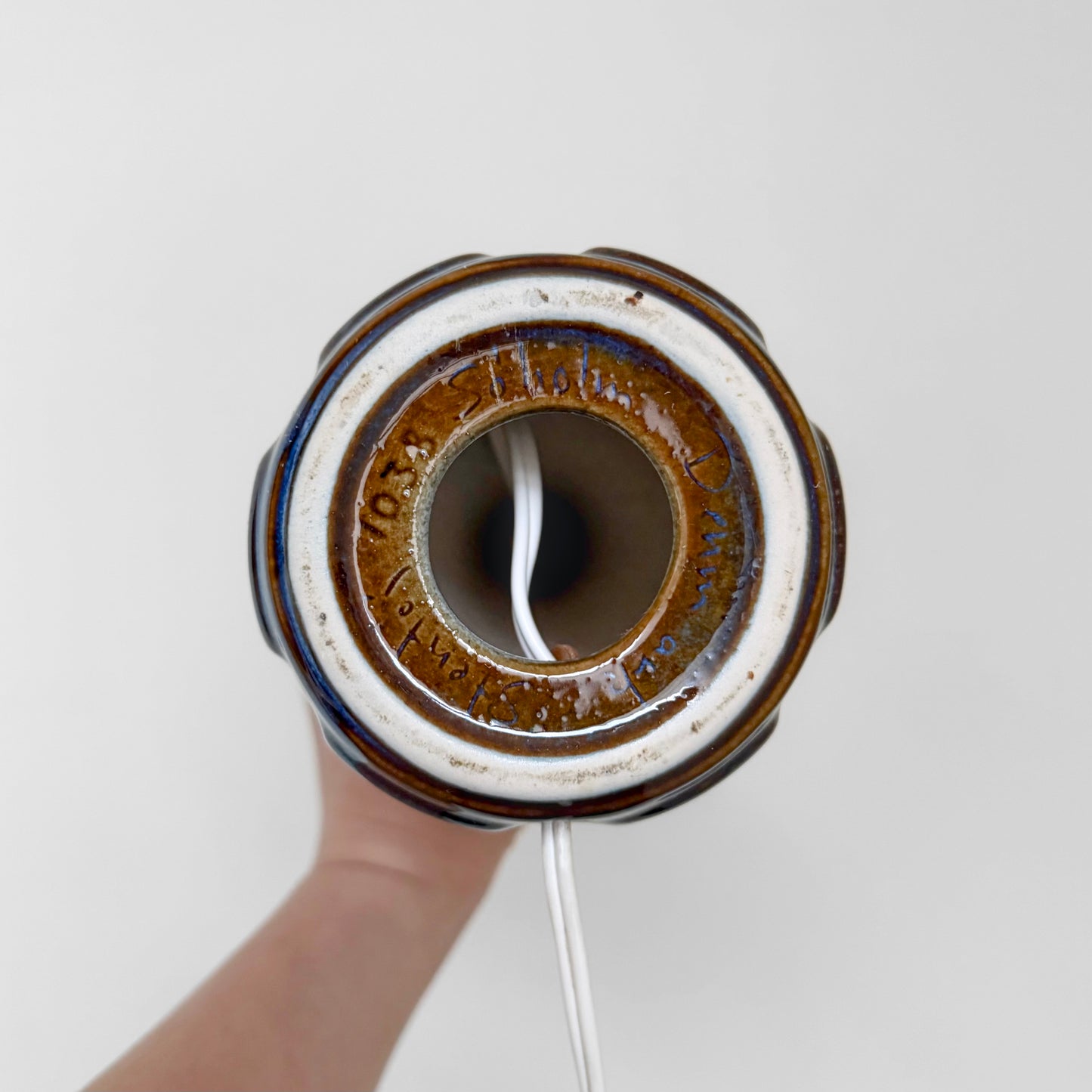View from above of the base of the Søholm 1038 Blue Stoneware Table Lamp showing the ceramic material, brown glaze, and underside markings while held by a hand against a white background.