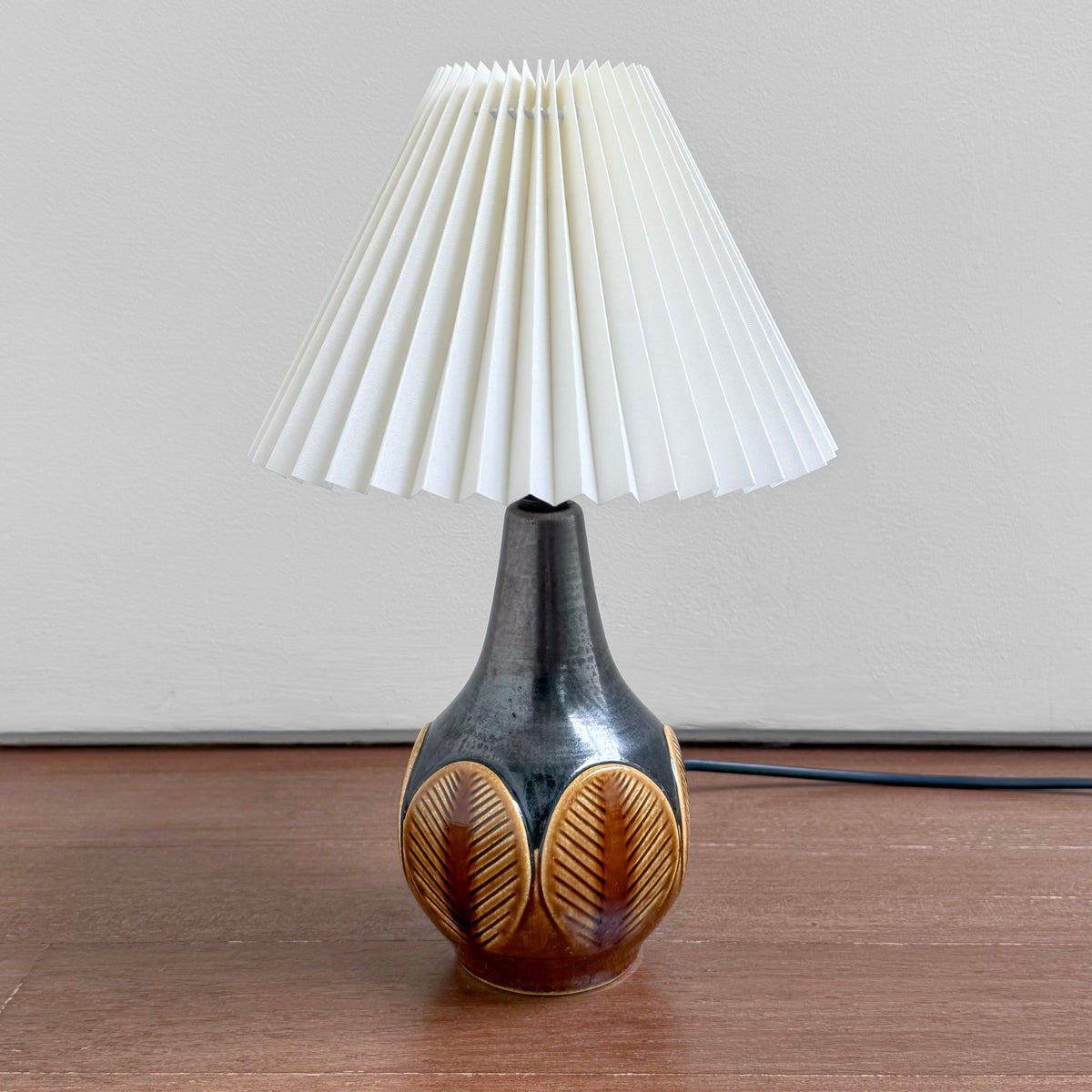 Søholm 1048 Black-Brown Stoneware Table Lamp with leaf relief ceramic base and white pleated shade on a wooden surface
