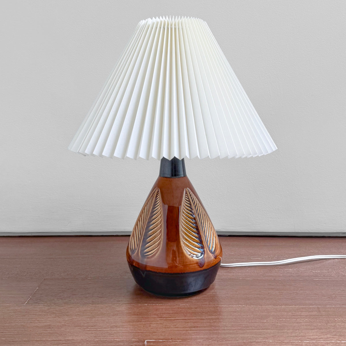 Søholm 1049 Brown-Black Stoneware Table Lamp with leaf relief, brown and black glaze, and a white pleated shade on a wooden surface