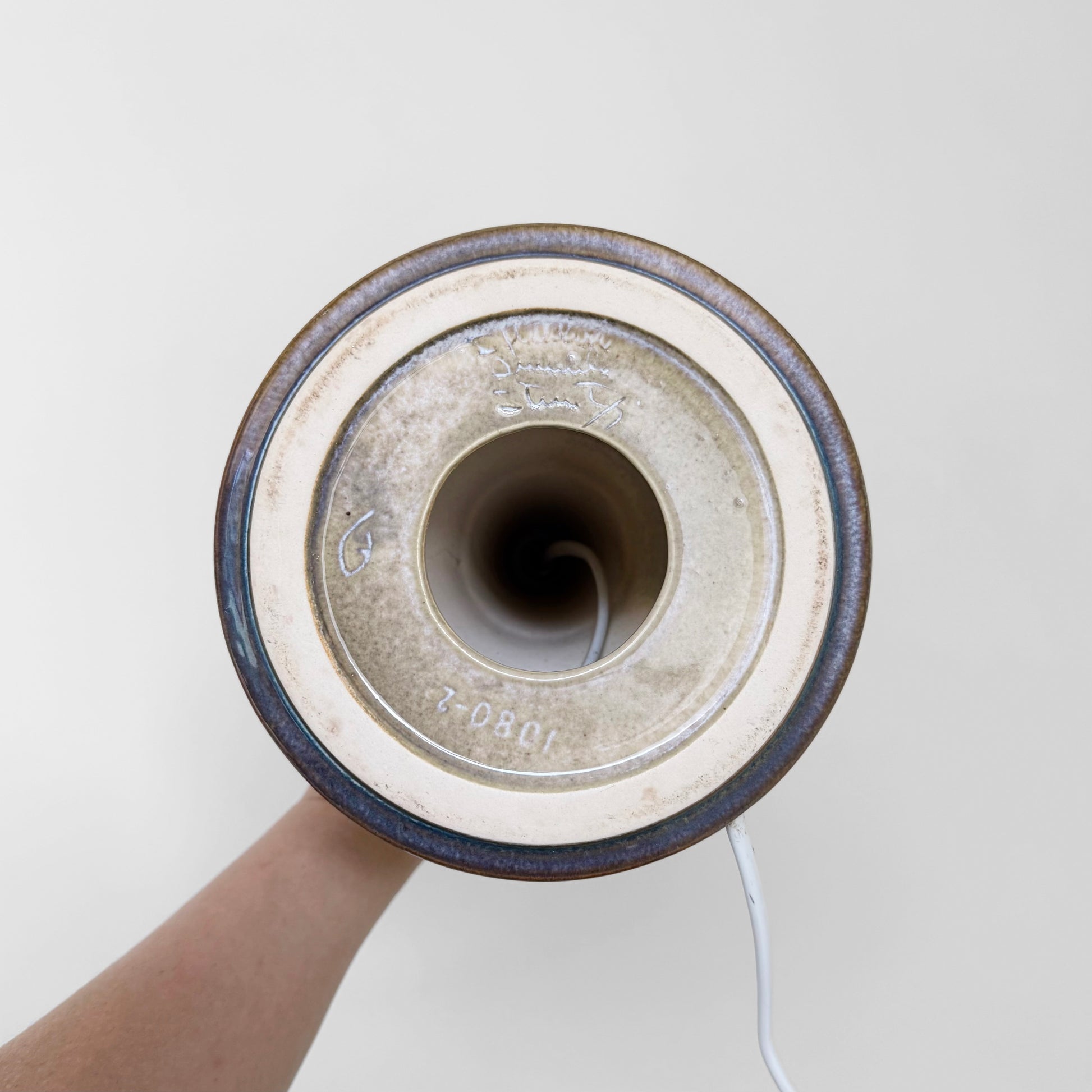 Underside view of the Søholm 1080 Dark Blue Stoneware Table Lamp showing ceramic base with model number and maker’s mark, held by a hand against a plain background.