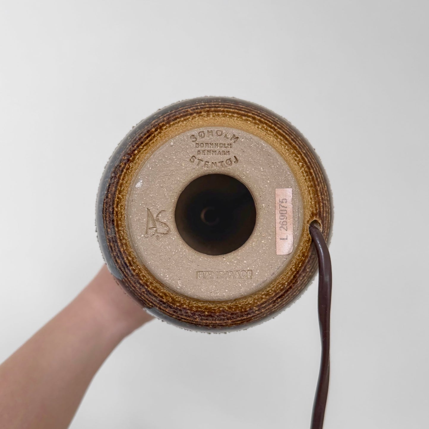 Bottom view of the Søholm Black-Brown Stoneware Table Lamp showing the ceramic base with maker's stamp, signature 'AS', and attached electrical cord.