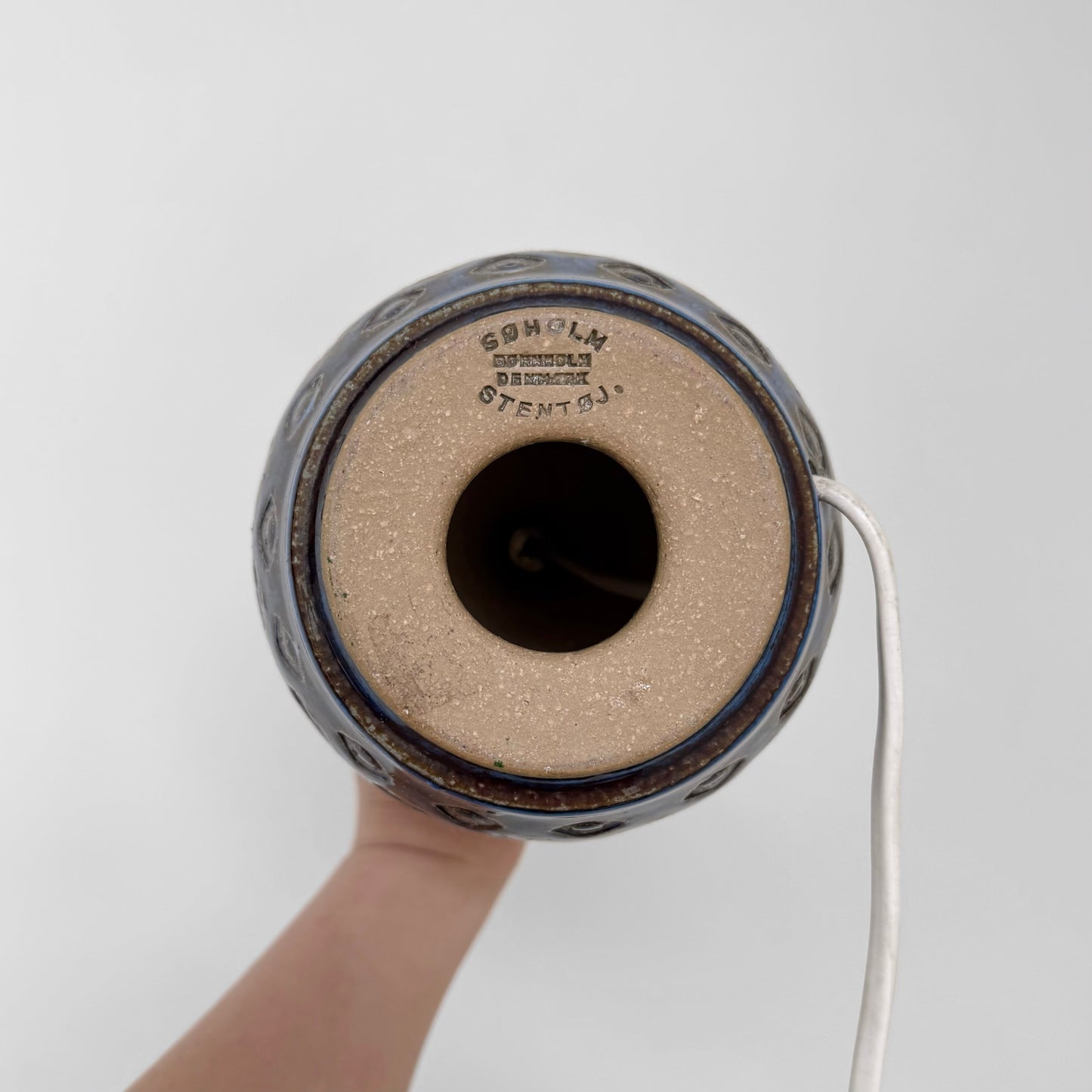 Bottom view of a Søholm Blue Stoneware Table Lamp showing the maker’s stamp on the ceramic base with a white electrical cord extending from the side.