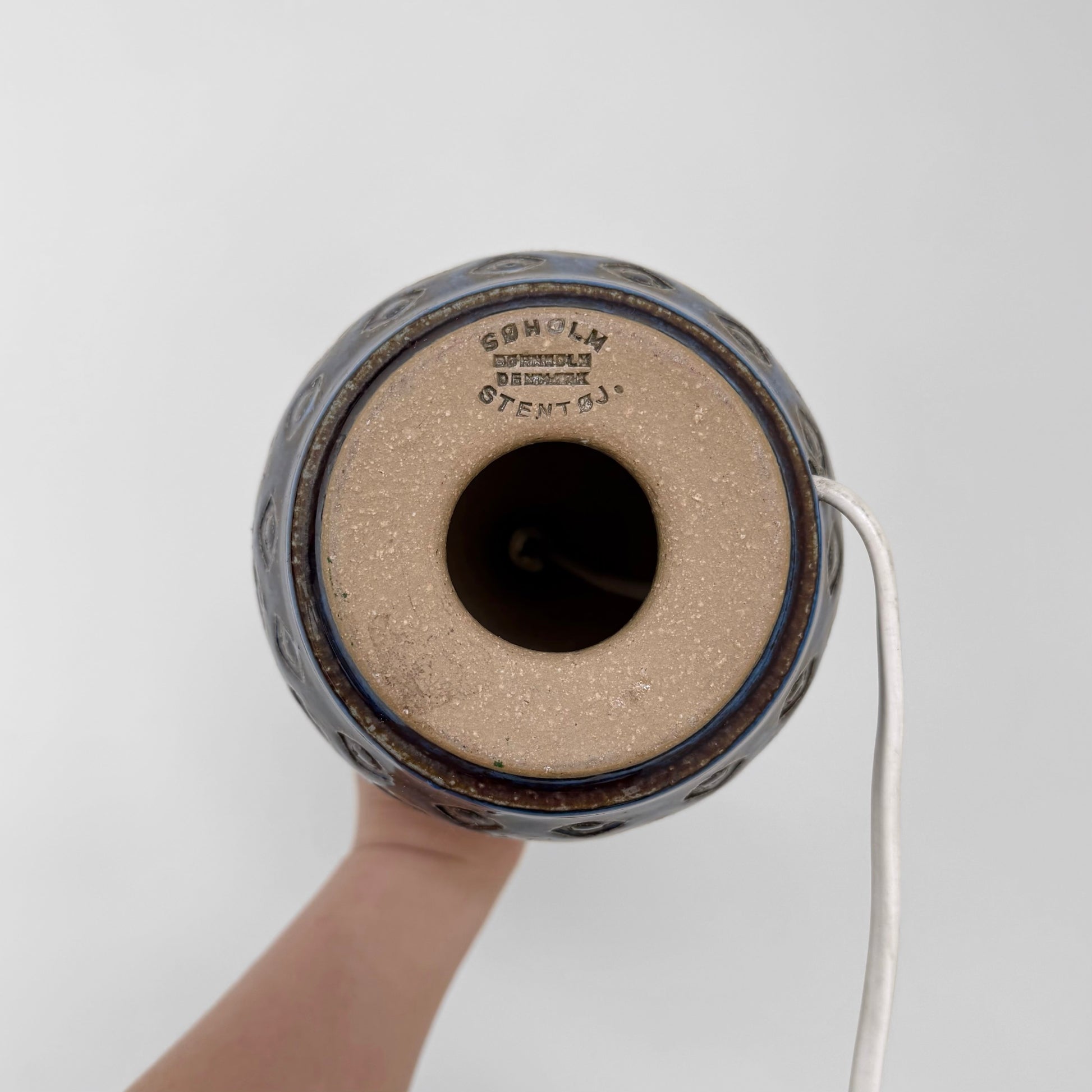 Bottom view of a Søholm Blue Stoneware Table Lamp showing the maker’s stamp on the ceramic base with a white electrical cord extending from the side.
