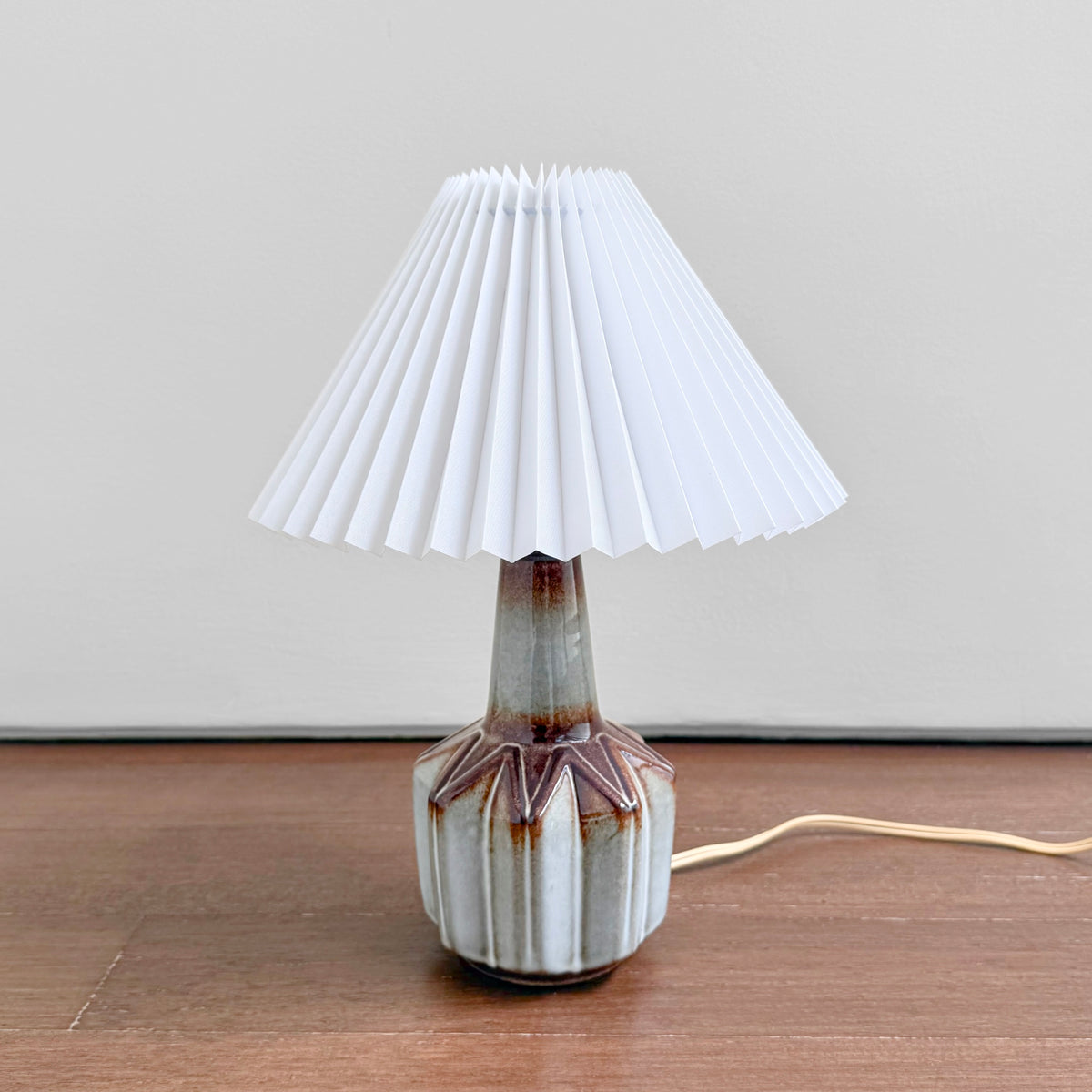 Søholm Grey-Brown Stoneware Table Lamp with a white pleated shade and multitone glazed ceramic base on a wooden surface