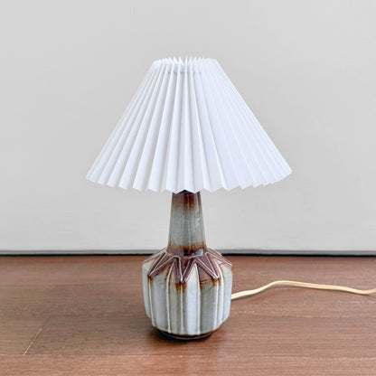 Søholm Grey-Brown Stoneware Table Lamp with a white pleated shade and multitone glazed ceramic base on a wooden surface