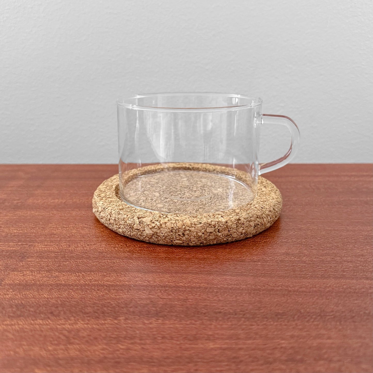 Signe Persson-Melin Boda Nova Glass Tea Cup with Cork Coaster featuring a clear glass cup with handle resting on a round natural cork coaster, displayed on a wooden surface.