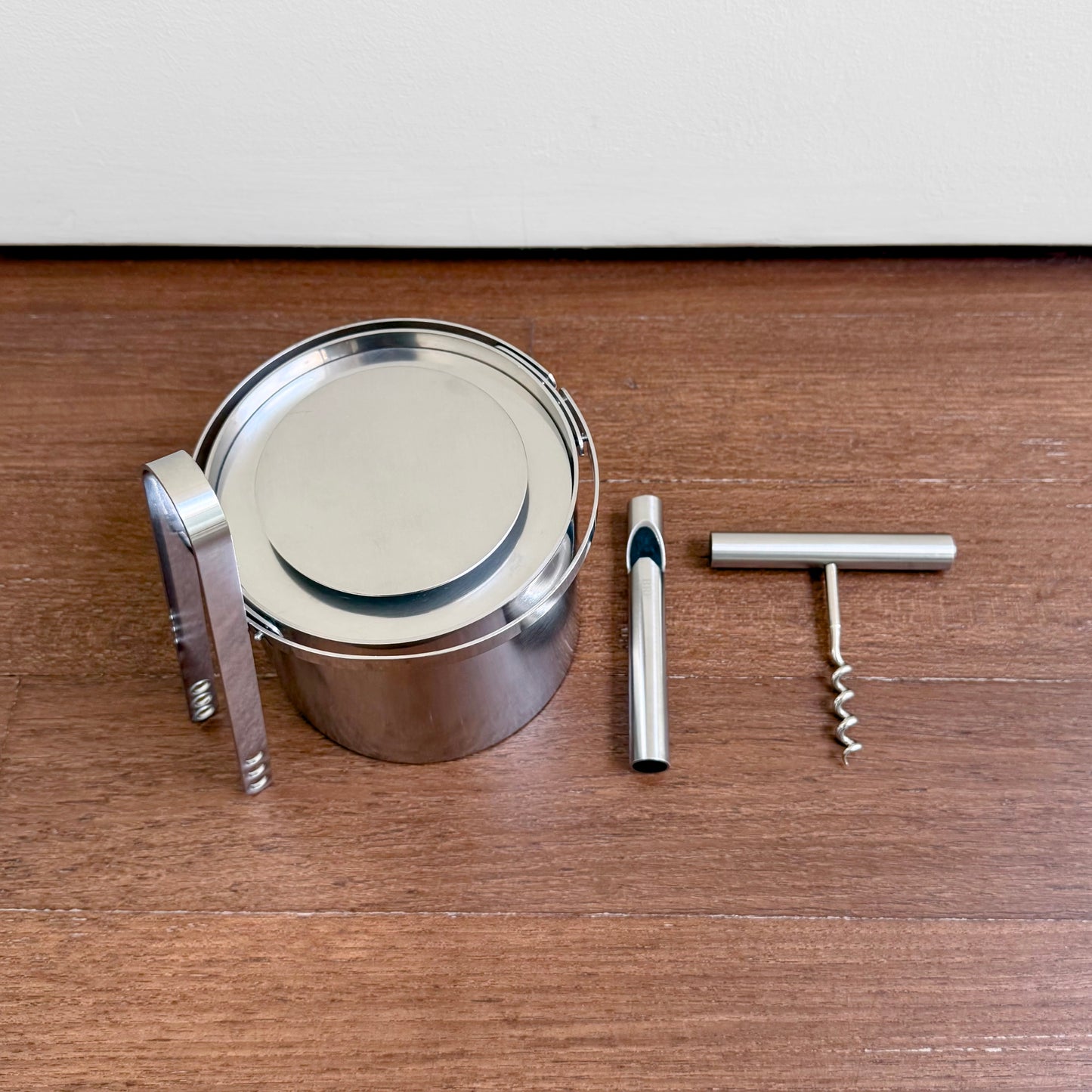 Vintage Stelton Stainless Steel Bar Set featuring a cylindrical ice bucket with tongs, a bottle opener, and a corkscrew in polished metal finish.