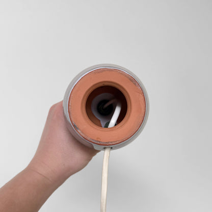 Swedish Small Botanical Table Lamp shown from below with its ceramic base opening and white electrical cord held by hand