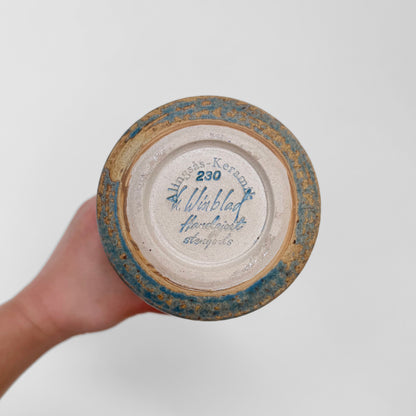 Hand holding the bottom of a Ulla Winblad Alingsås Keramik Stoneware Vase showing the maker's stamp and handwritten details on ceramic surface with blue and beige glaze.
